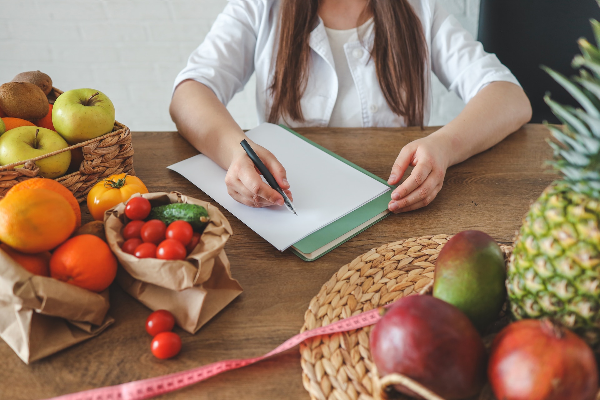 Doctor nutritionist writing case history in the office. Young woman dietitian prescribing recipe